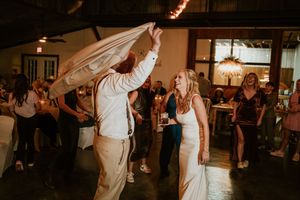 Bride and groom dancing together at wedding reception with guests celebrating in background.