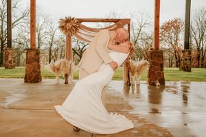 Bride and groom share a romantic dip kiss on a rainy outdoor wedding venue with pampas grass decor.