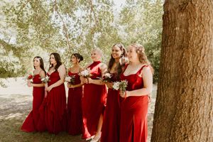 Bridesmaids in red dresses standing in a row outdoors holding bouquets.