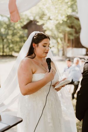 Bride in white dress reading vows during outdoor ceremony.