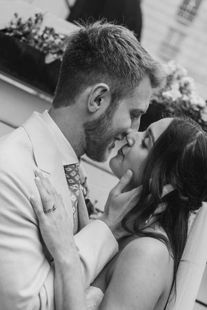 Black and white photo of a smiling couple sharing a romantic moment, nearly kissing at their wedding.