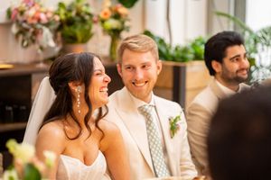 Smiling bride and groom in elegant wedding attire seated together during their indoor wedding reception ceremony.