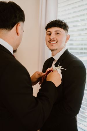 Getting ready scene with formal black suit and boutonniere being pinned.