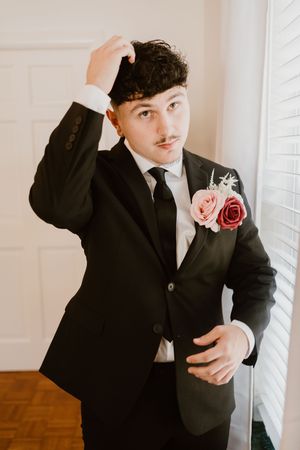 Black and white formal portrait of groom adjusting tie before ceremony.