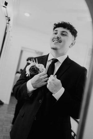 Artistic black and white shots of groom preparing with boutonniere and formal attire.