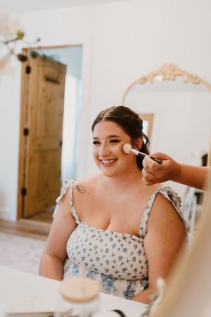 Getting makeup applied while wearing a floral print top during wedding preparation.