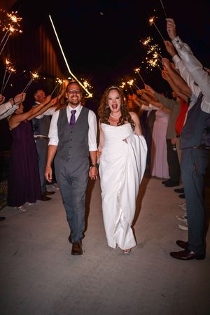 Bride and groom walk through sparkler tunnel at night during wedding reception exit.