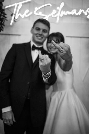 Black and white wedding photo with neon sign and couple showing off rings.