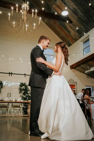 A romantic first dance between newlyweds in an elegant venue with chandeliers and exposed beams.