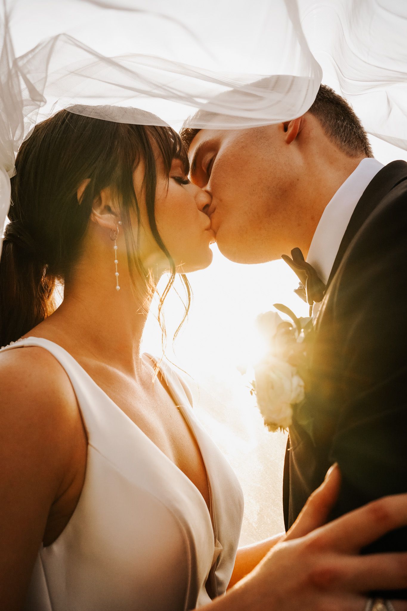 Romantic wedding moment captured in golden sunlight with flowing veil.