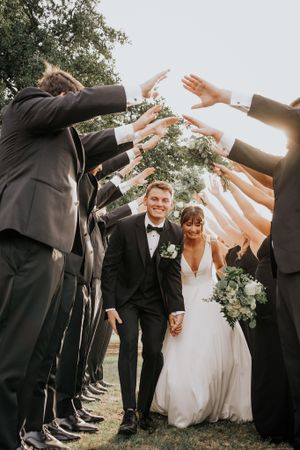Wedding party forms a tunnel of raised arms for the newlyweds to walk through.