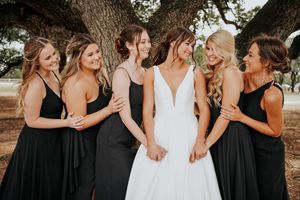 Bridesmaids in black dresses pose together with the bride in white for a wedding photo.