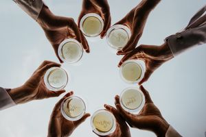 Aerial view of hands holding white coffee cups in a circle against light background.