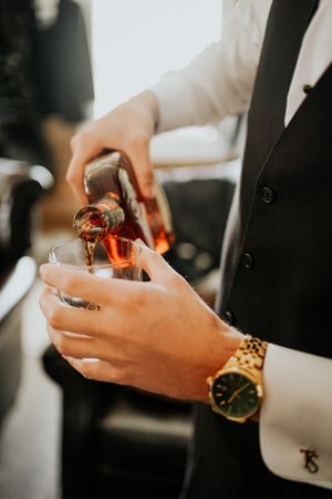 Hands pouring champagne or wine into glass with gold watch detail.