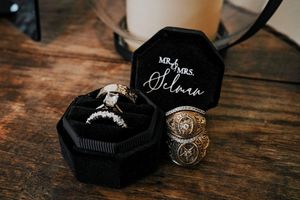 Wedding rings displayed in black octagonal box on wooden surface.