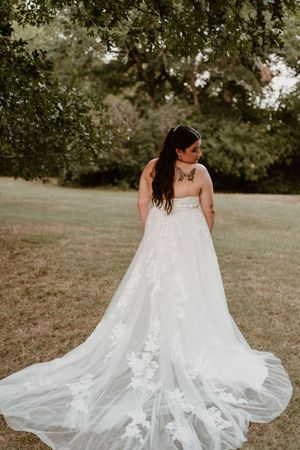 Wedding dress detail shots showing intricate lace and flowing train on grassy background.