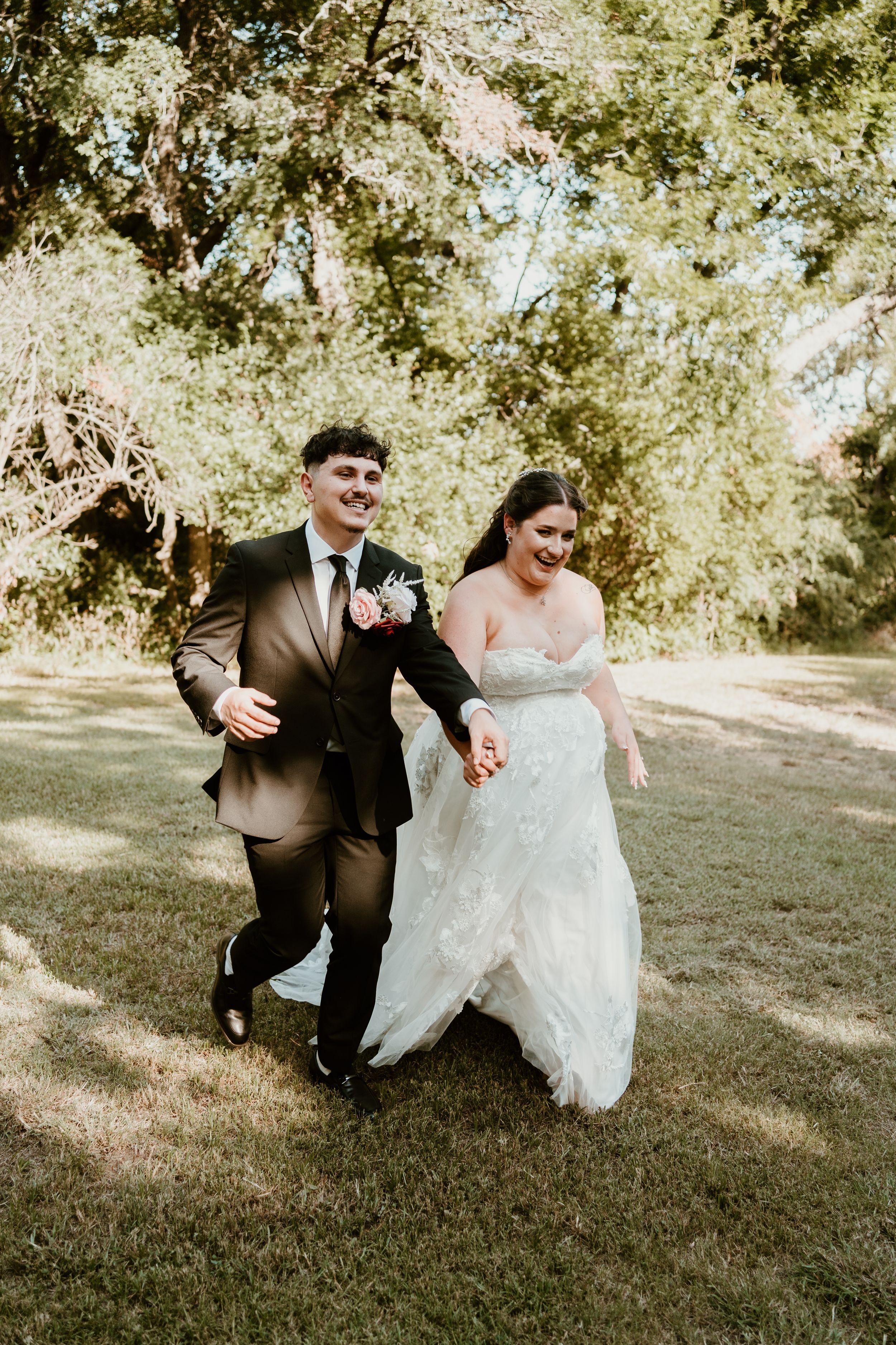 Playful wedding couple runs and poses on grassy hill in formal attire.