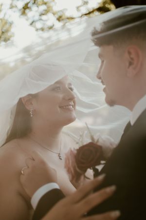 A romantic wedding couple shares intimate moments under a flowing veil during their outdoor photoshoot.