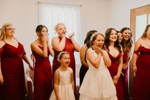 Wedding party wearing burgundy and cream colored dresses standing together indoors.