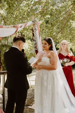 Wedding party members gather under trees during an outdoor ceremony.