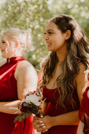 Bridesmaids in burgundy dresses laughing together during outdoor wedding celebration.