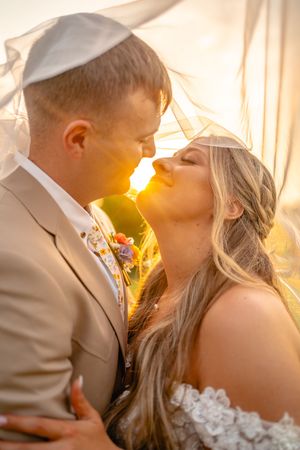 Bride and groom share a romantic moment under a veil at golden hour sunset during their wedding.