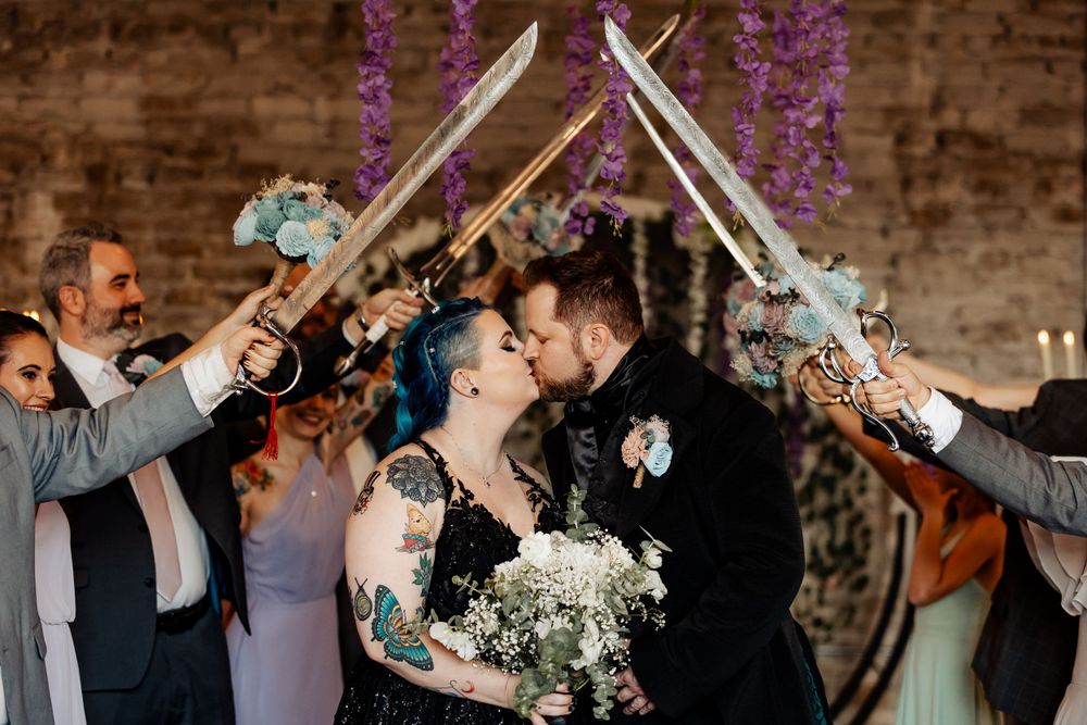 Wedding ceremony exit with guests holding crossed swords while couple shares a kiss.