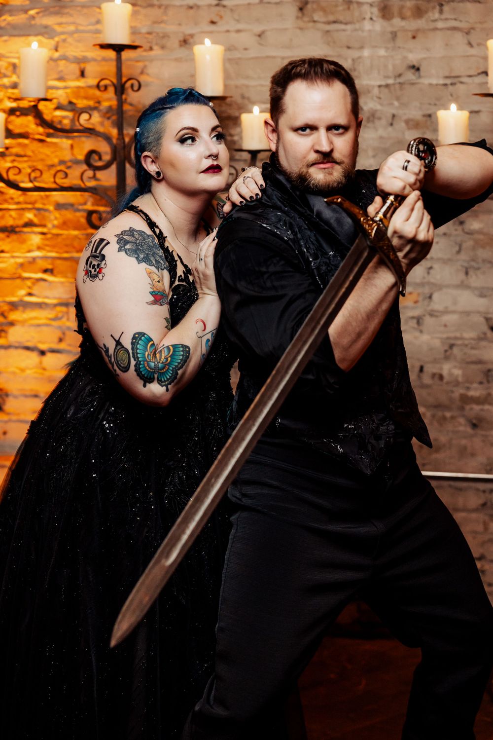 A dramatic medieval-themed wedding portrait with couple posing with a sword against brick wall.