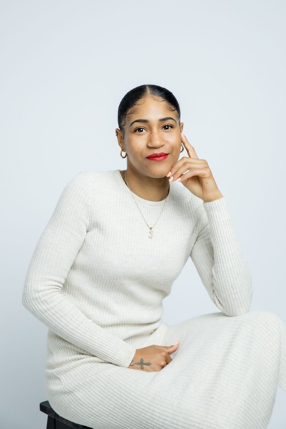 A person in a cozy white ribbed sweater dress poses against a light background while touching their face.