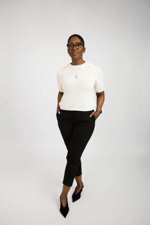 Professional studio photo showing a white knit top paired with black cropped pants and pointed heels against a light background.