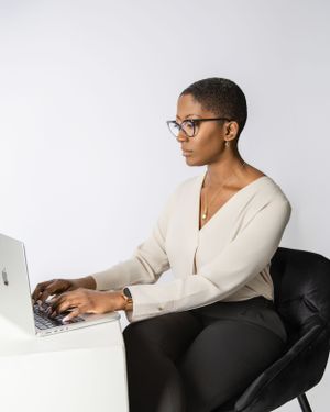 Professional working at a laptop while sitting in a modern black chair wearing a cream sweater and glasses.