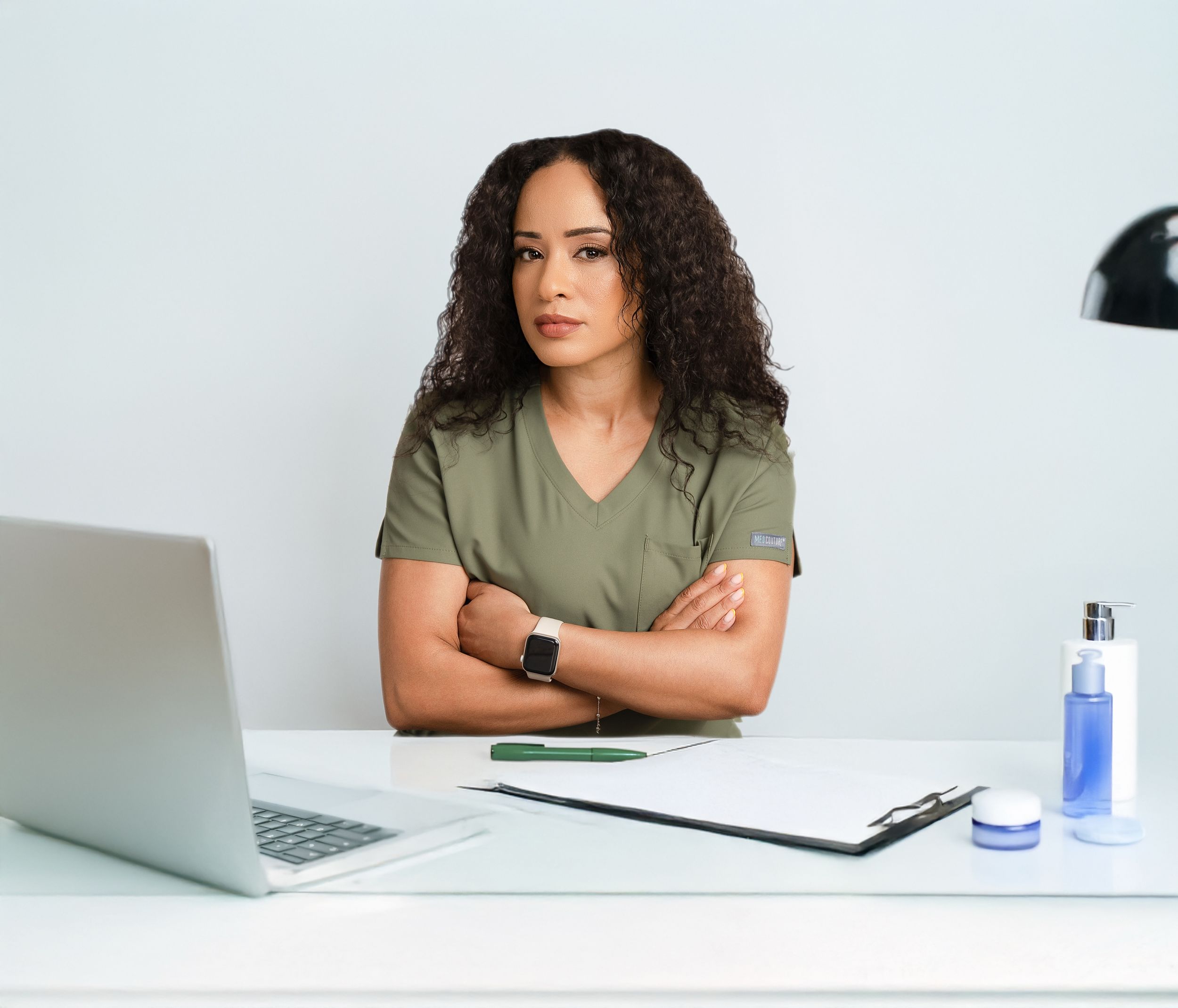 Someone sitting at desk with laptop, water bottle and notebook while wearing olive green top.