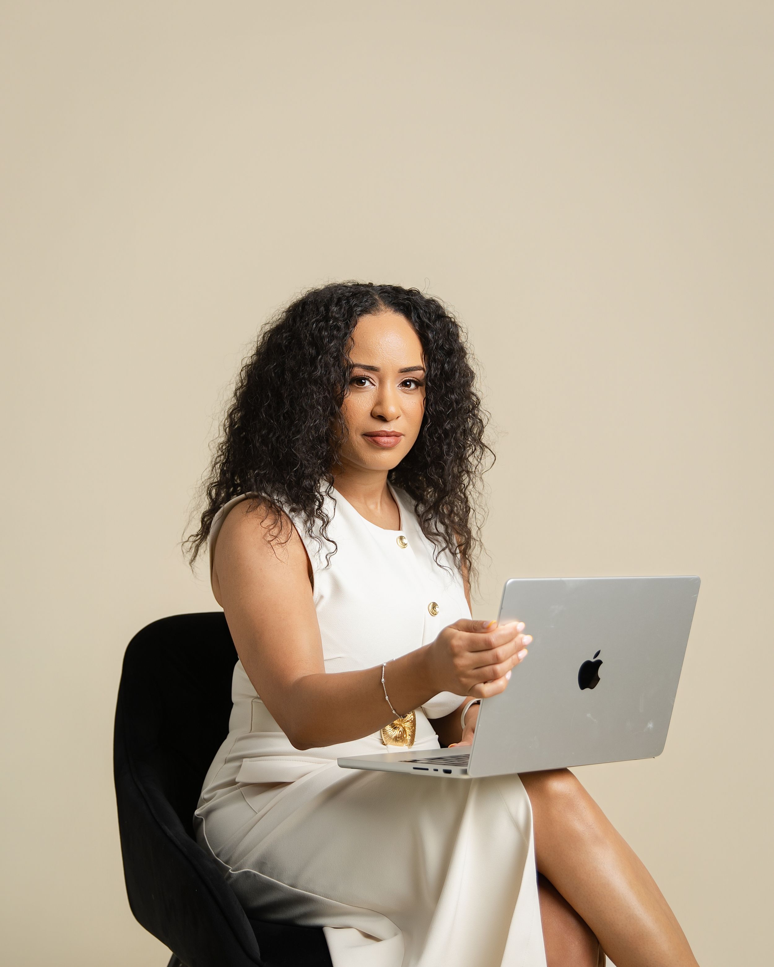 Professional in white dress working on MacBook laptop while seated in office chair.