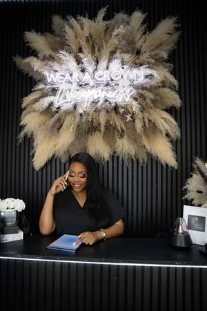 Professional receptionist in a black top works at a modern desk with a pampas grass decorative display and neon sign above.