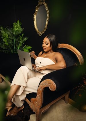 Lifestyle photo of entrepreneur working on laptop in elegant vintage chair with gold mirror and plants. at Vanessa Charlotte Photography stu