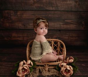 Boho-inspired milestone baby portrait in Brooklyn, NY, with a green romper, wicker chair, and delicate floral accents.