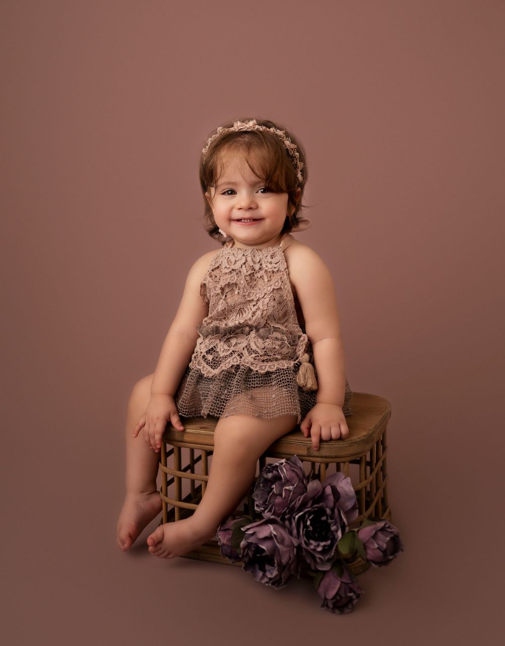 Vintage-inspired baby portrait in Brooklyn, NY, featuring a little girl in a lace romper on a warm brown backdrop for a timeless look.