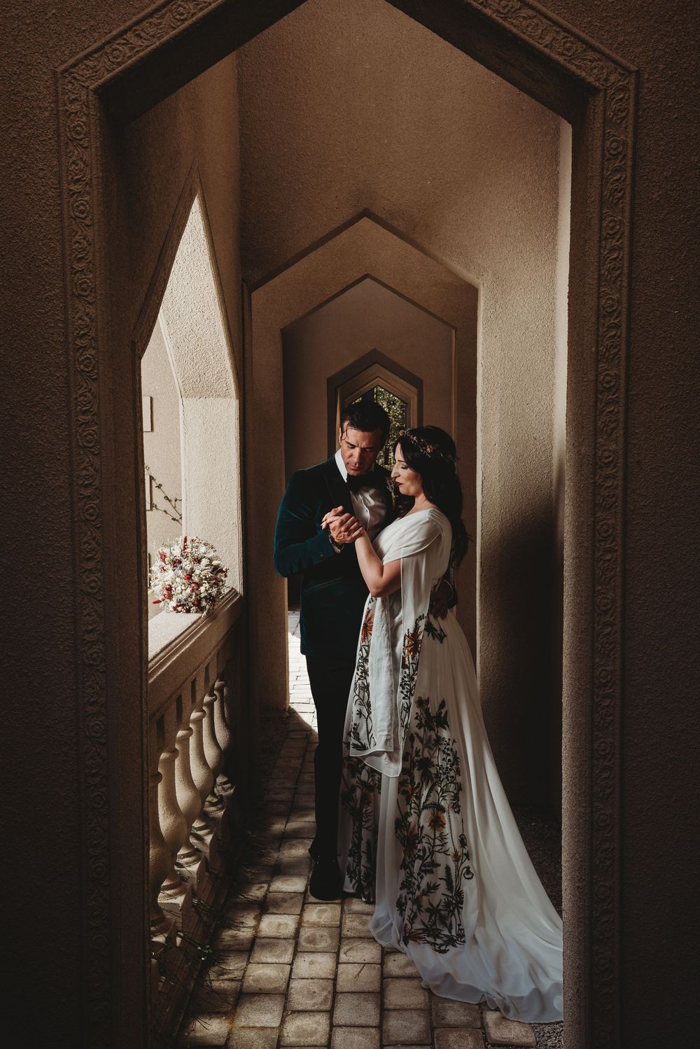 Bride and groom share intimate moment in ornate Moroccan-style arched hallway of wedding venue.