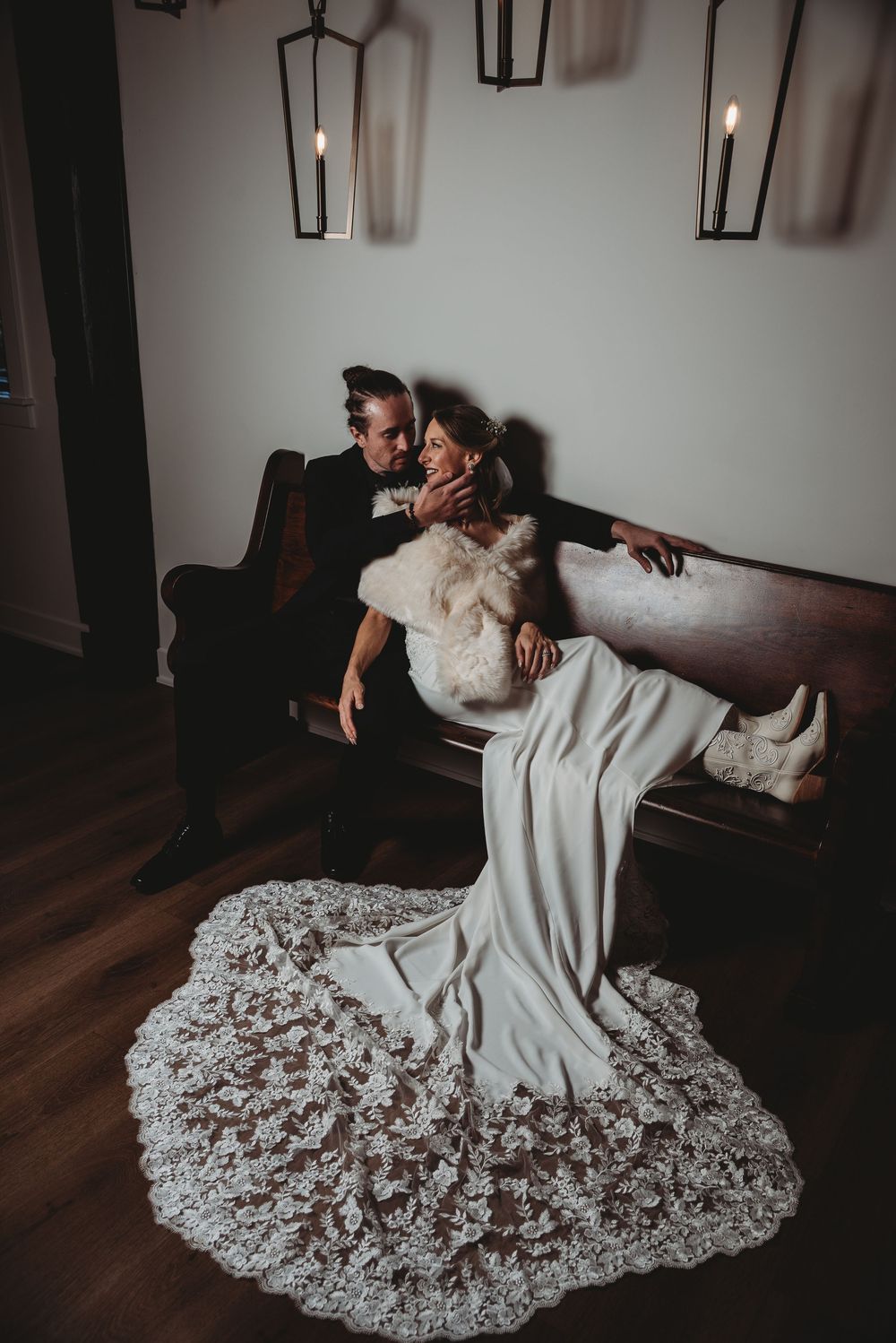 Bride and groom share intimate moment on vintage sofa, her lace cathedral train spread elegantly.
