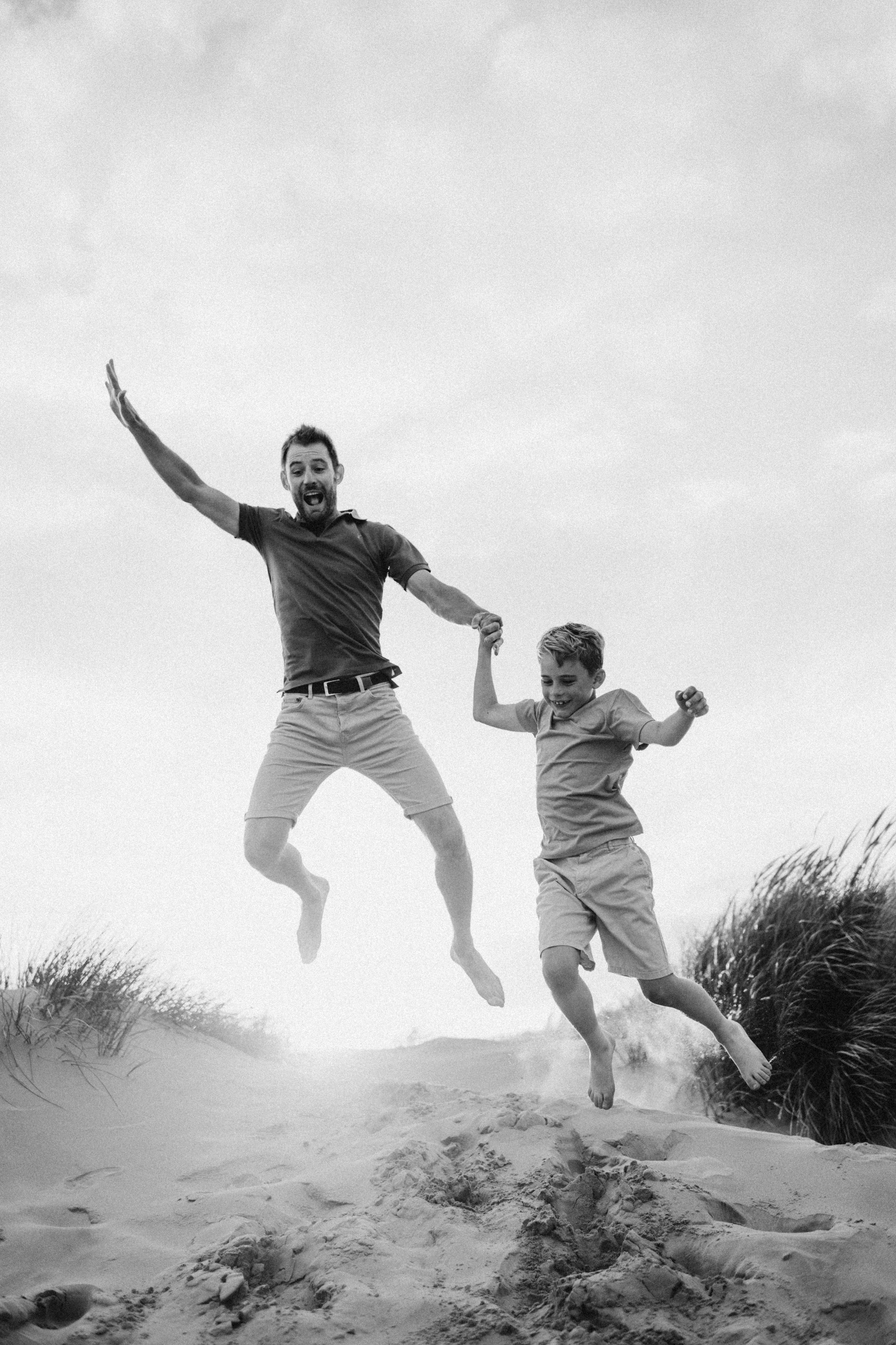 a dad and his son jumping in the sand during a photo session in Kent