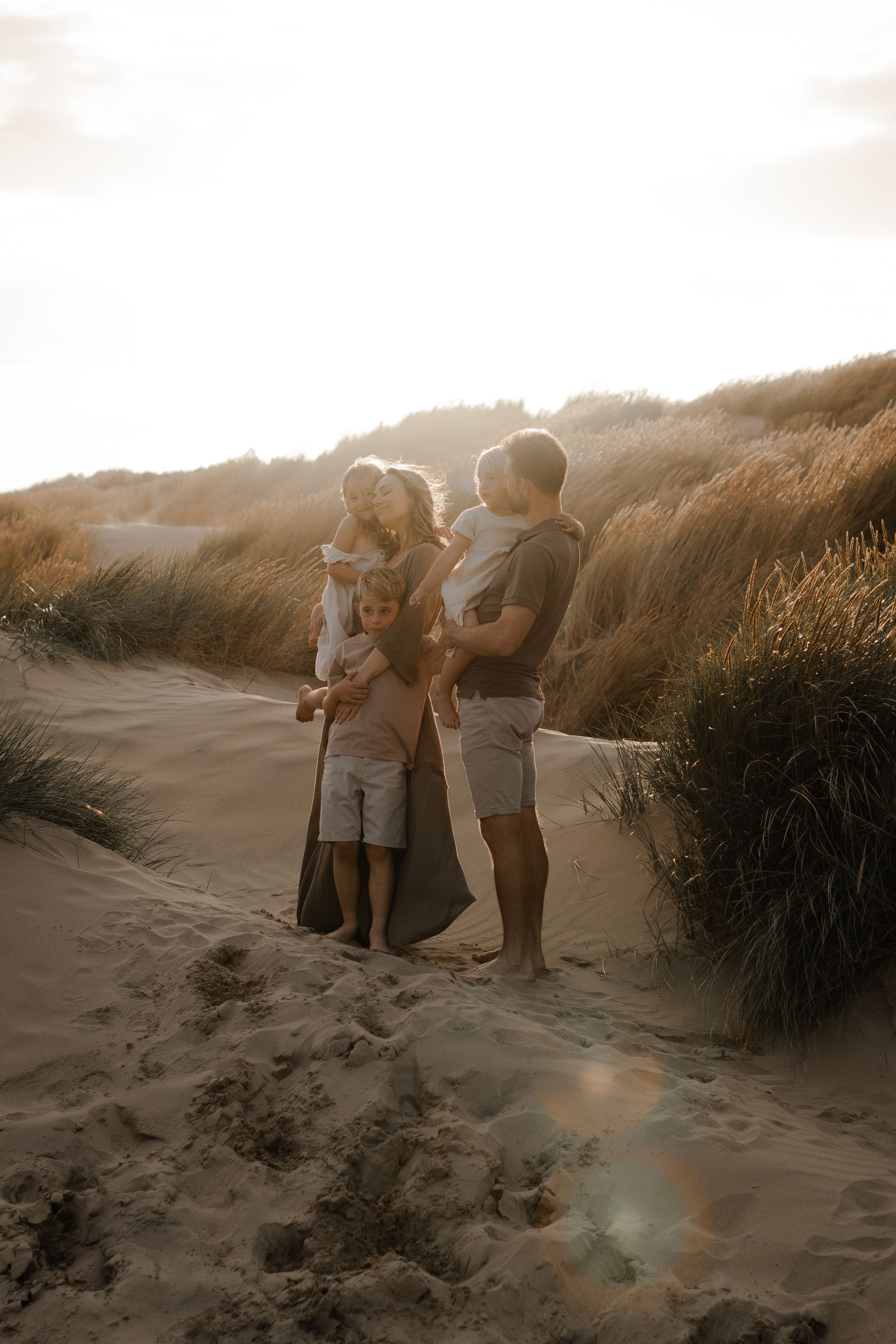 a family standing on a sand dune at sunset during a photo session in Kent