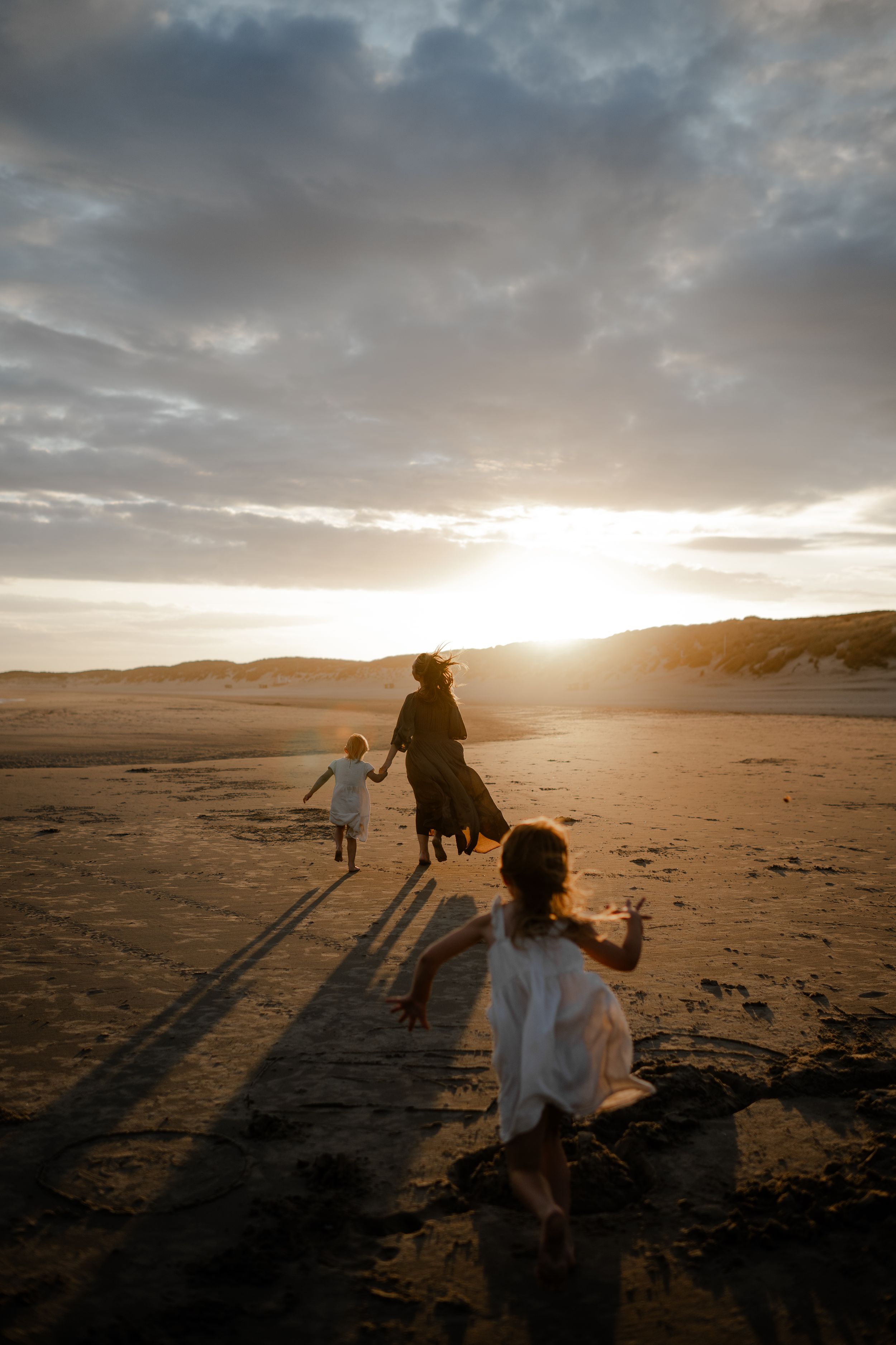 a mother running towards the sunset with her girls by her side during a photo session in Kent