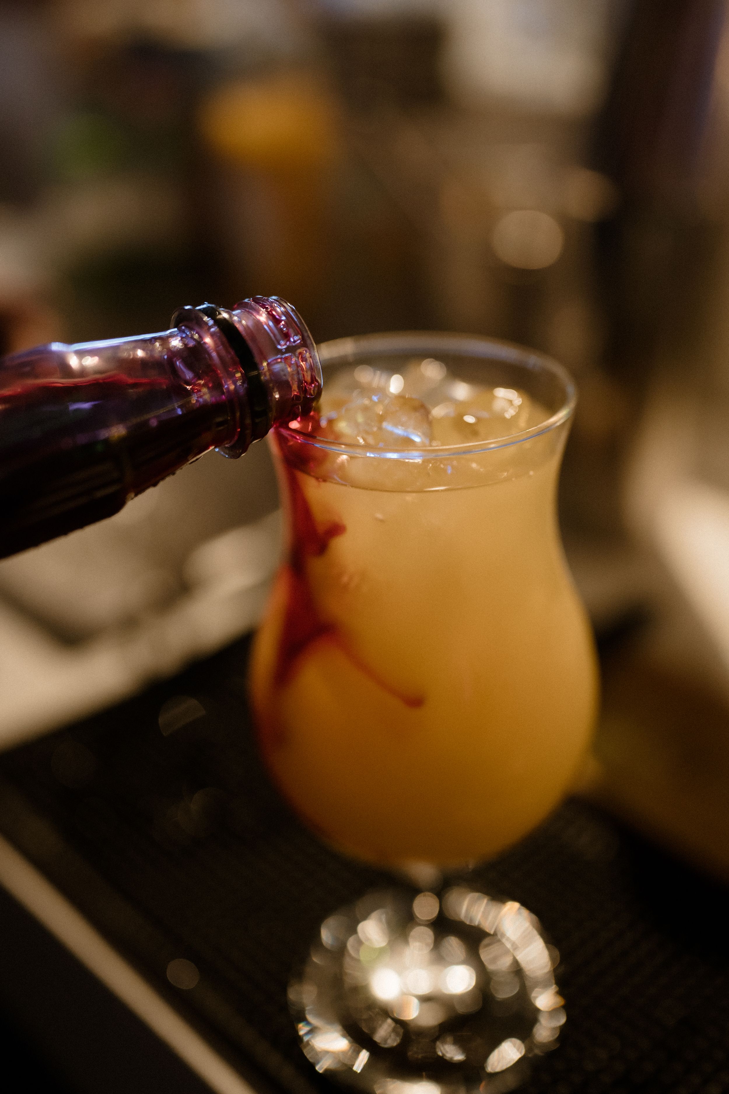 Red wine being poured into a golden cocktail creating an artistic swirl effect.