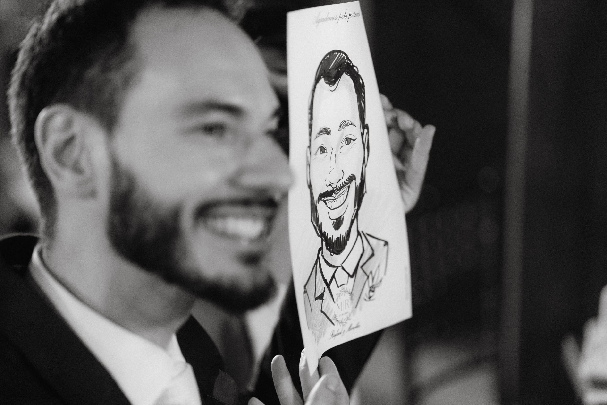 A caricature drawing is held up next to the subject in black and white photography.