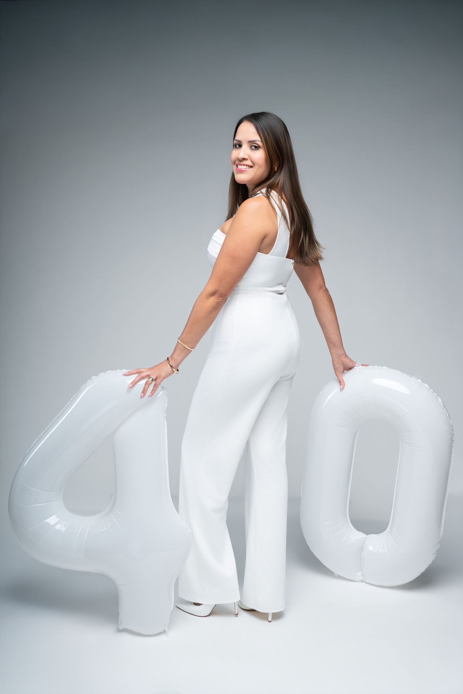 Woman in white jumpsuit posing with large white number 40 balloons, celebrating her 40th birthday.