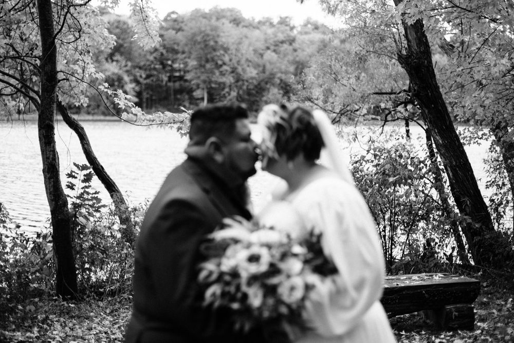 A romantic black and white wedding photo by a lake with trees framing the couple.
