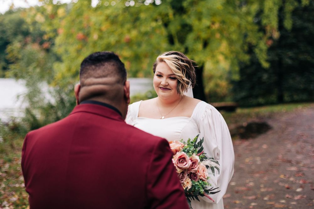 A couple shares a romantic moment during a fall wedding photoshoot by a lake with colorful autumn foliage.