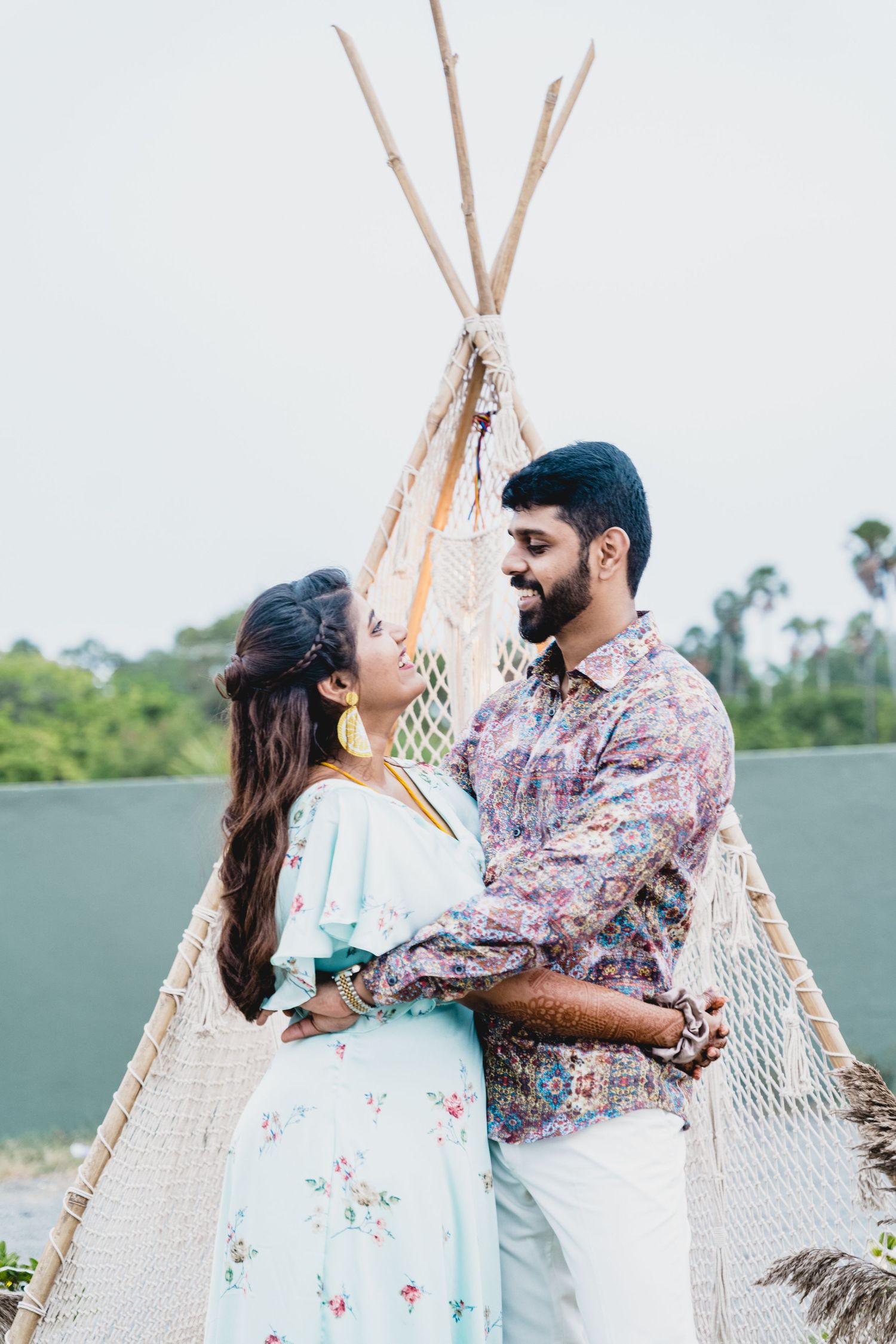 Couple shares intimate moment near decorative teepee structure in casual outfits.