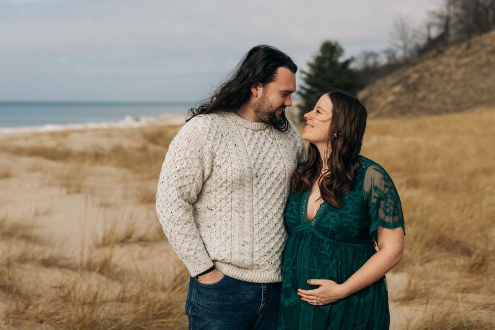 Couple in casual winter clothing stand together on beach dunes.