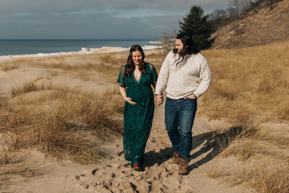 Two people walk together on a sandy beach path near Lake Michigan on a cloudy day.